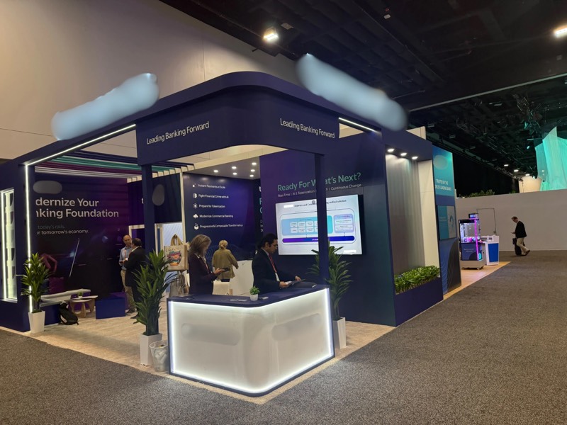 Corner view of the navy custom exhibition stand with an illuminated white reception counter at SIBOS 2026, Miami